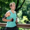 Man jogging outdoors wearing a turquoise tank top and armband.