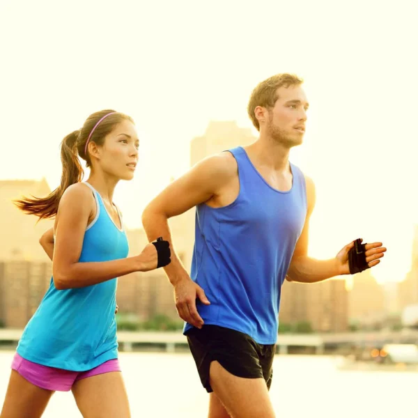 A man and woman jogging outdoors in athletic wear at sunrise.